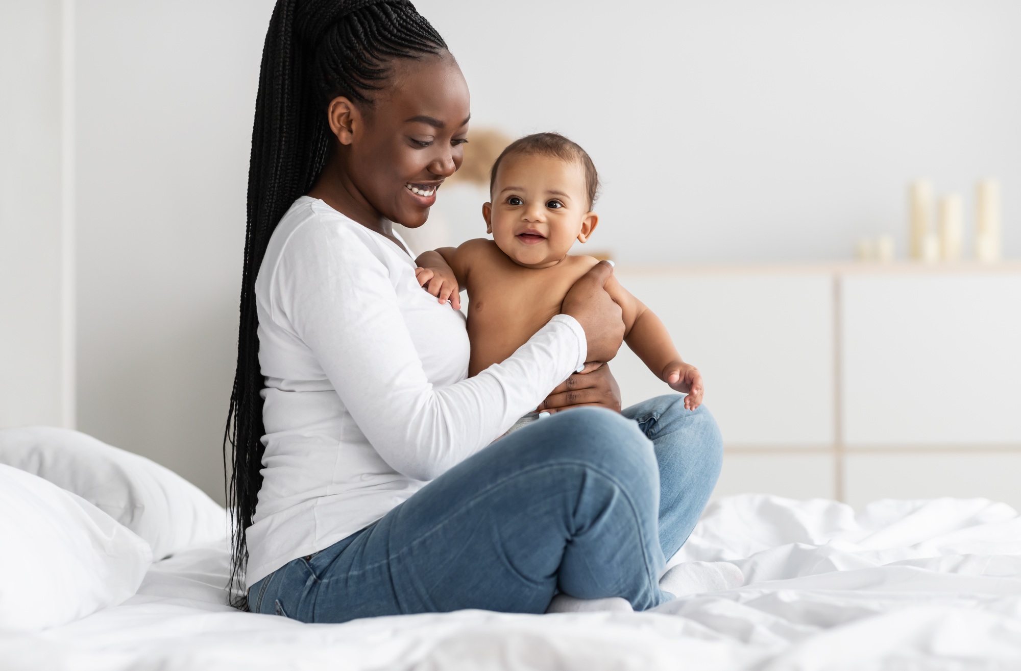 Black nanny sitting on bed with her cute baby