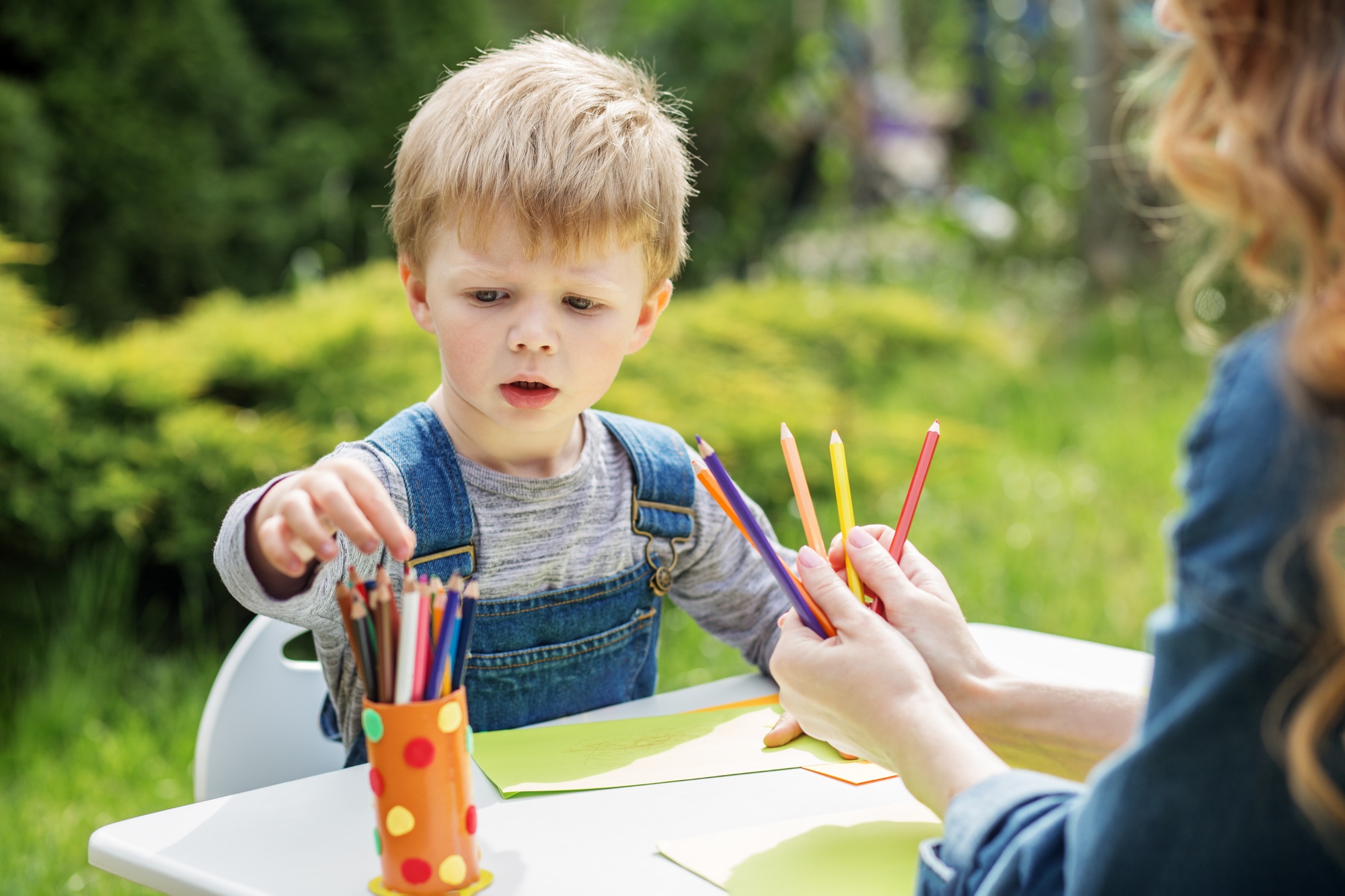 Child selecting colored pencils in garden. Early years. Baby development.