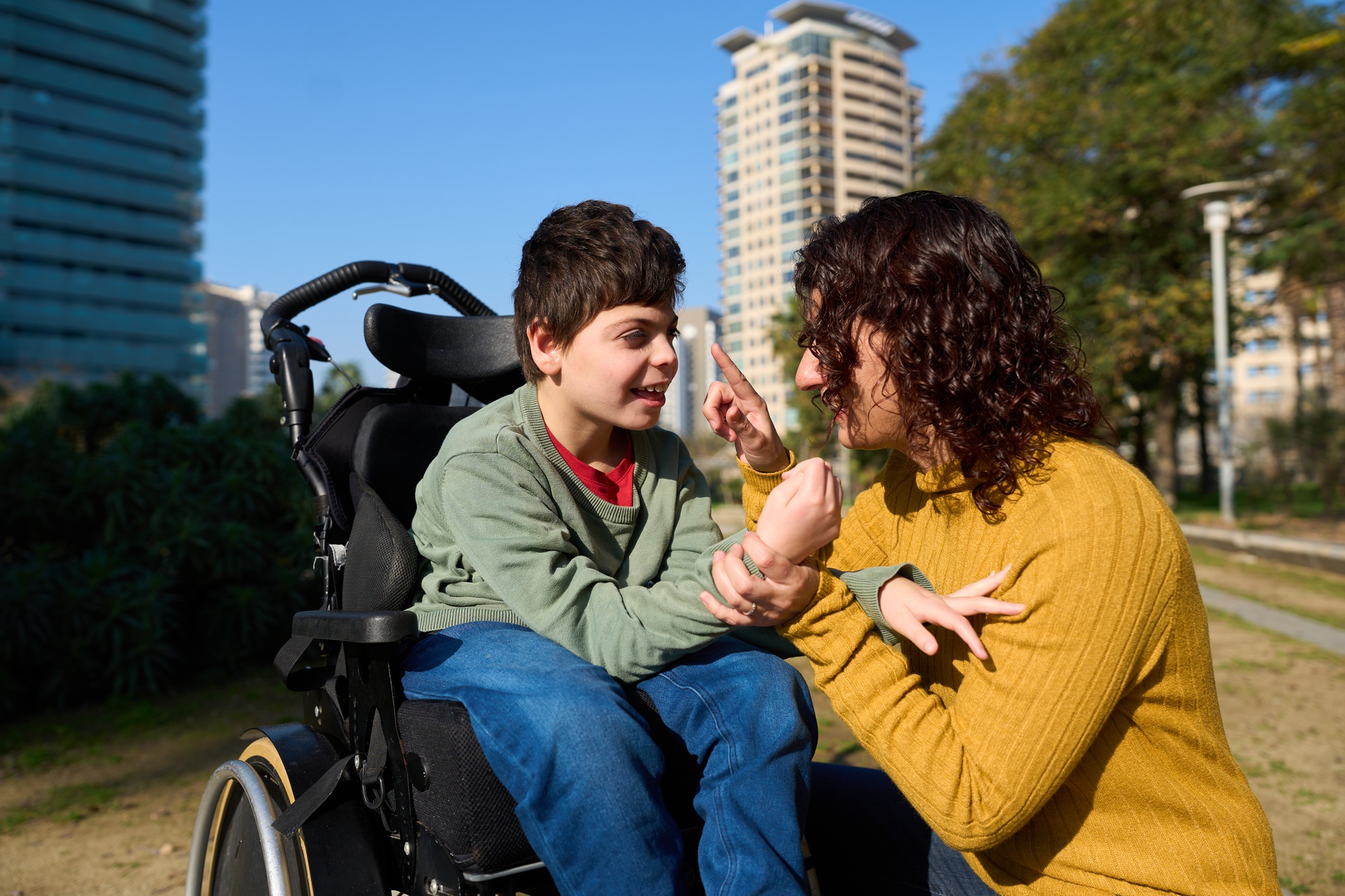 Happy child with disability communicating with special needs educator outdoors - cerebral palsy